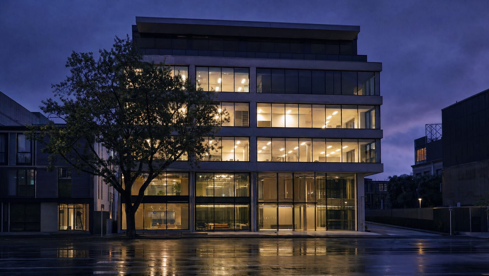 A mid-rise New Zealand commercial building at dusk, seen from the street with its floors lit