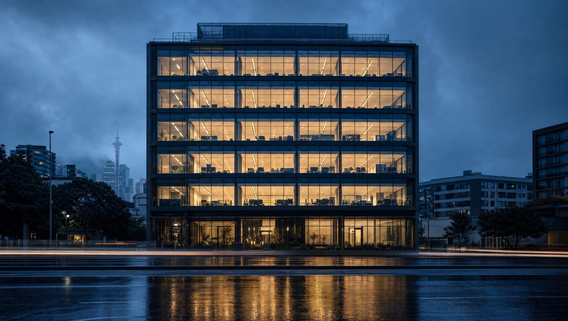A six-storey glass office building on a wet Auckland street at blue hour, every floor lit.