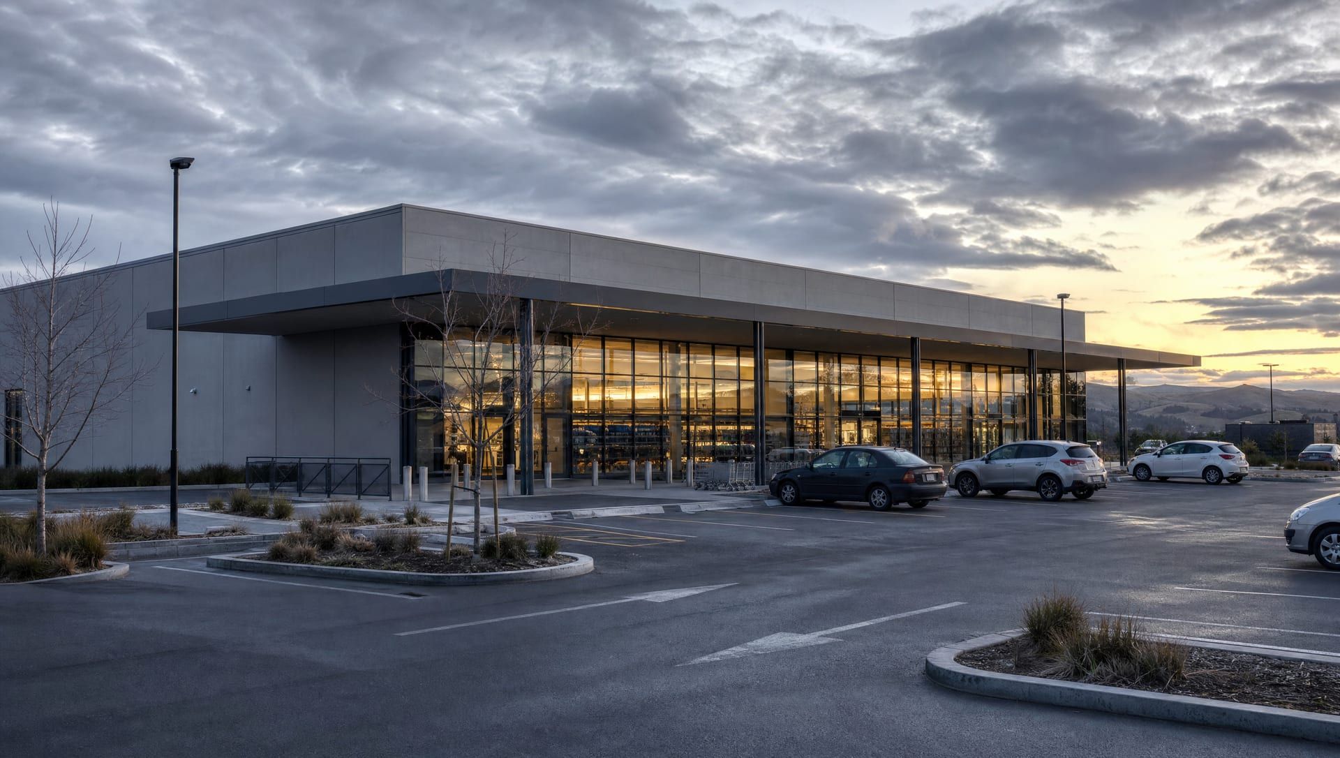 A large-format standalone retail store in late afternoon, a tall glazed shopfront under a flat canopy, cars in the car park.